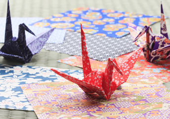 Origami paper cranes perch on colorful paper.