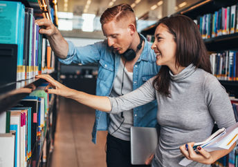 Two young students getting books from a public library shelf.