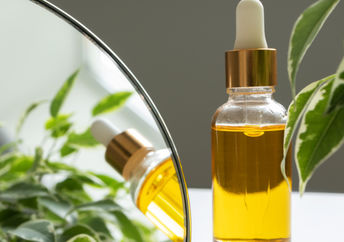 A bottle of vitamin E oil, nourishing for skin and hair, is beside a makeup mirror.
