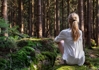 Woman sitting in green forest enjoys the silence and beauty of nature