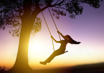 Silhouette of joyful woman on a swing with sunset background