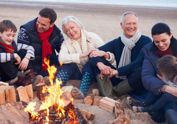 Grandparents, parents, and children connect by enjoying time together around a beach bonfire.