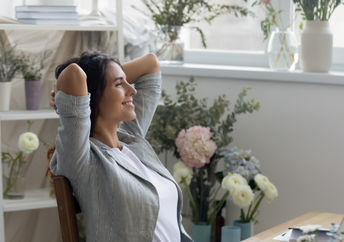 A woman feels calm and relaxed in her mindful workspace surrounded by flowers and soft colors.