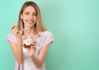 A young woman is eating a gut-healthy breakfast of yogurt with fruit.