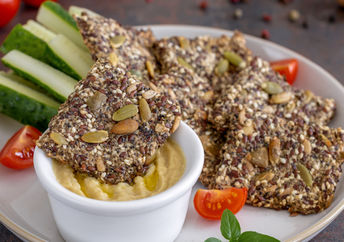 Homemade seed crackers are served with hummus and fresh vegetables.