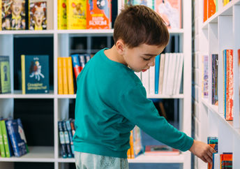 An eight-year-old boy adding his own book to the library bookshelf.