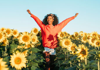 A woman joyfully walks through a field of sunflowers.