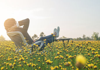 Businessman sitting in an office armchair and relaxing in a yellow flower field.