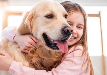Little girl hugging her golden retriever dog and smiling.