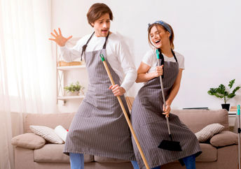 Cheerful couple having fun and dancing while spring cleaning their home.