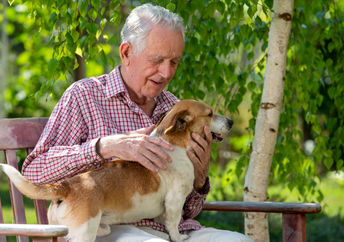 Senior man cuddling a dog outside.