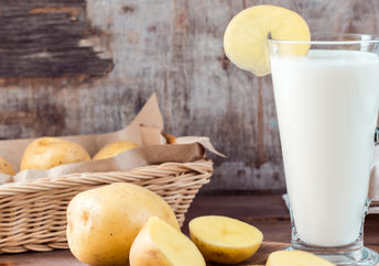 A glass of healthy potato milk is placed beside sustainable potatoes.