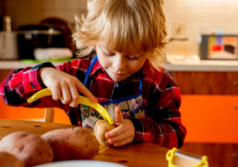 A little kid is carefully peeling potatoes in her kitchen.
