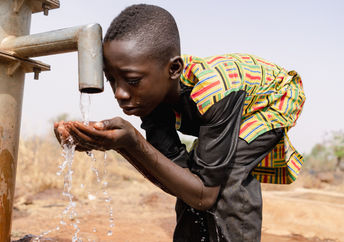African boy drinking water from a tap.