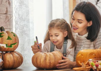 A mother carves a pumpkin for Halloween with her young daughter.