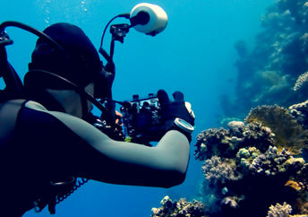 Scuba diver taking pictures on a coral reef surrounded by the blue ocean, tropical corals and fish.