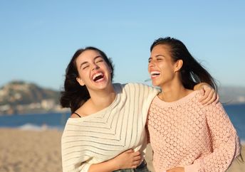 Two friends laugh while walking on the beach.