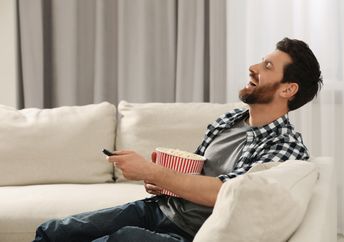 A man laughs while watching TV.