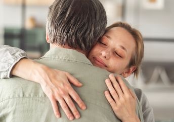 An adult daughter hugs her father.
