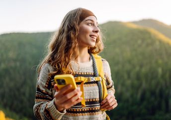 Alt: A woman walks in nature while holding her phone.