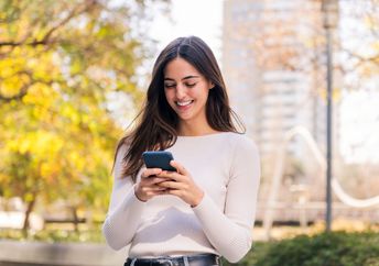A woman smiles while she uses her phone.
