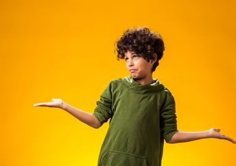 A boy keeps his arms to the side and shrugs.