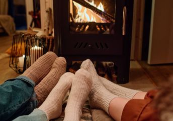 Three people wearing cozy socks sit together on the floor in front of a fireplace in a home.
