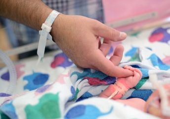 A first-time dad holds the tiny finger of his newborn who needed a little help breathing so was in the NICU.