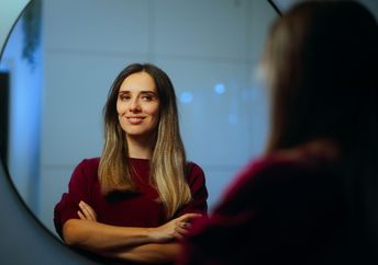 A happy woman smiles while she looks at herself in the mirror.