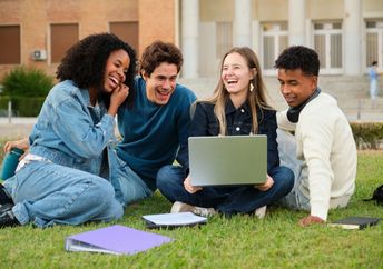 A diverse group of young adults sitting on the grass and smiling.