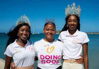 Three women wearing tiaras and Good Deeds Day shirts stand by the water.