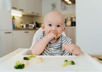 A baby boy eats vegetables.