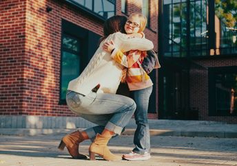 A mother kneels down to hug her daughter.