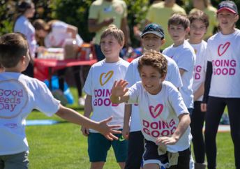 Children wearing “Doing Good” shirts run and play together at a community event.