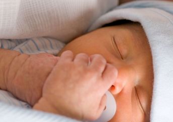 Newborn preemie holds his white pacifier.