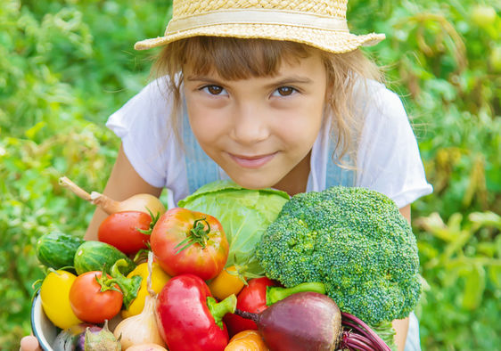 A young girl in a field holds a basket filled with freshly-picked vegetables.