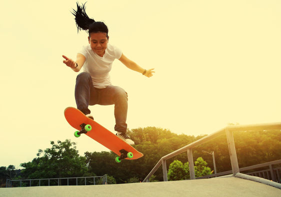 A smiling young girl does an ollie move at a skateboard park.
