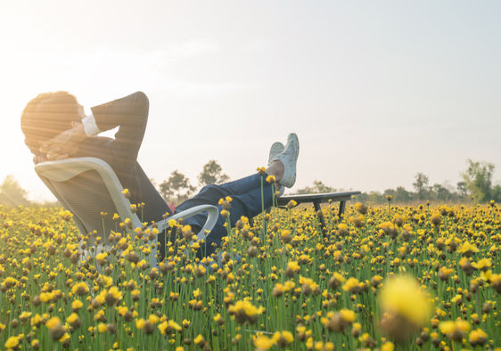 Businessman sitting in an office armchair and relaxing in a yellow flower field.