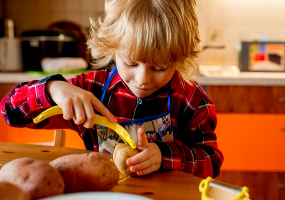 A little kid is carefully peeling potatoes in her kitchen.
