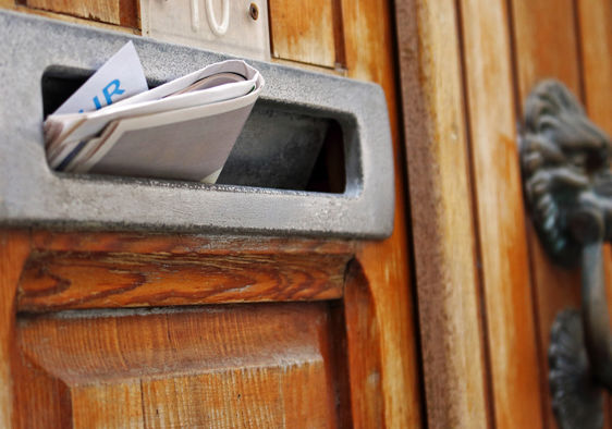 Mailbox filled with rolled spam newspaper in an old wooden door.