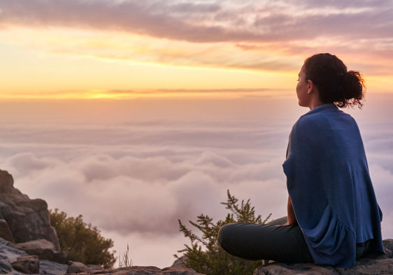 Woman sitting on a mountain top peacefully gazing at clouds