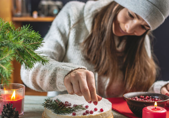 A woman decorating a festive cake with red berries.