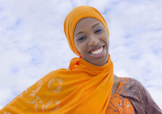 Joyful, young African woman wearing a traditional headscarf in the street.