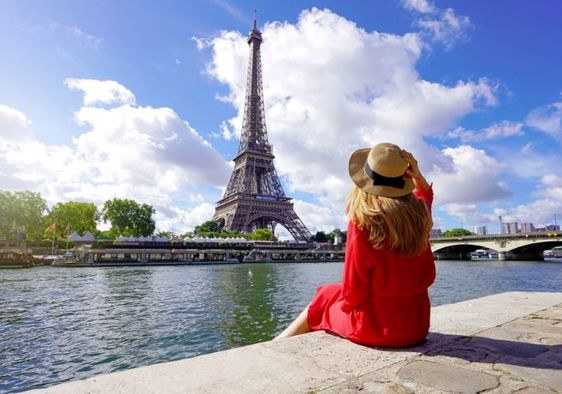 A woman sits on the quay of the Seine River looking at the Paris landmark Eiffel Tower.