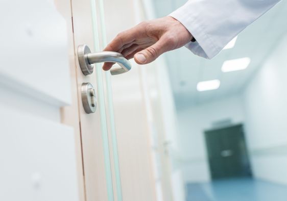 A doctor reaches for a door handle.