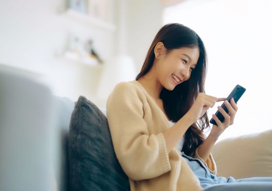 A woman sits on the couch using her phone.