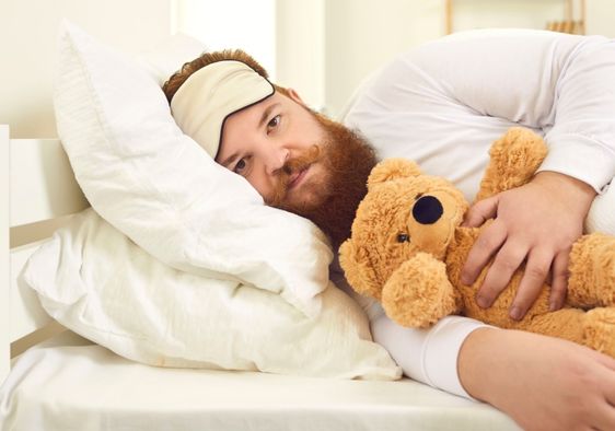 Adult man sleeping with a stuffed animal.