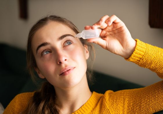 A woman using eye drops in a living room.