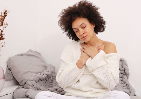 A woman sits with her hands on her chest.