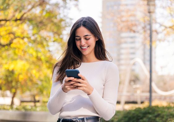 A woman smiles while she uses her phone.